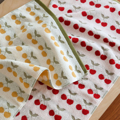 Red cherry patterned bath towel in the foreground, yellow cherry patterned towel in the background, showing the two color options of the Cherry Cotton Bath Towel Set