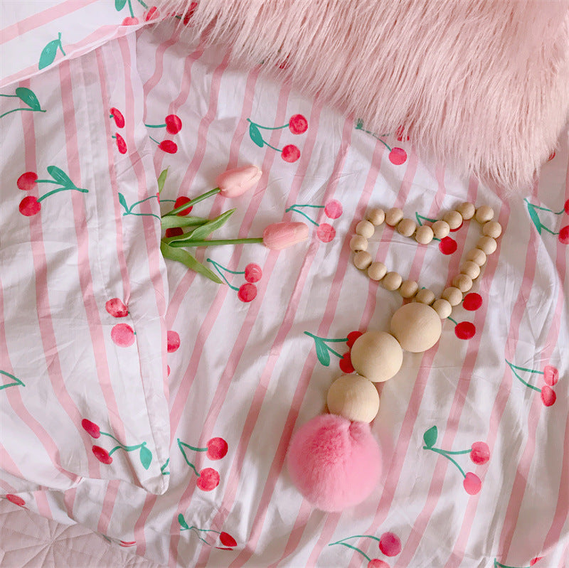 Wooden teething ring with pink pom-pom on a cherry-patterned fabric background