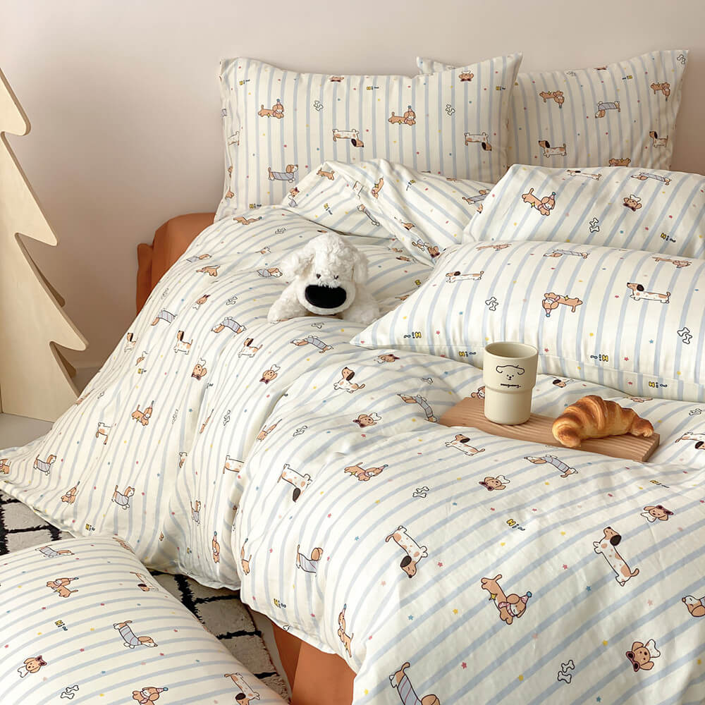 Dachshund kids bedding set styled on a bed with soft blue stripes, dog illustrations, matching pillows, and plush puppy decor