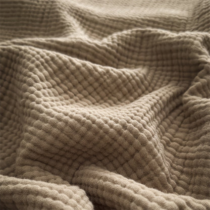 A detailed close-up shot of a beige 4-layer cotton muslin throw blanket with fringe, highlighting its soft, textured weave.