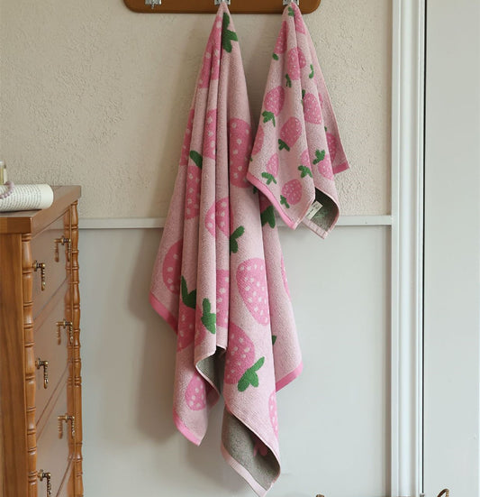 Pink strawberry cotton towel set hanging beside a wooden dresser
