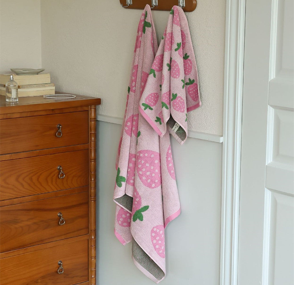 Pink strawberry bath towel and face towel hanging on wall hooks