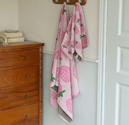 Pink strawberry bath towel and face towel hanging on wall hooks