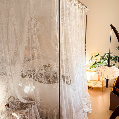 White lace curtains in a room with a table and lamp.