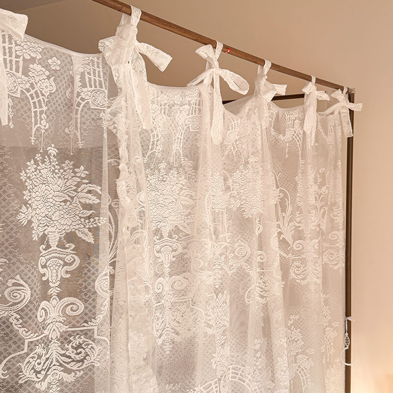 Lace curtains with floral patterns hanging on a rod against a beige wall.
