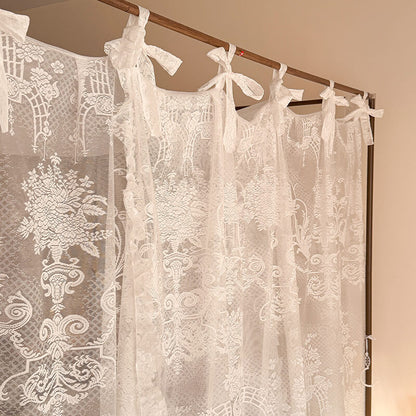 Lace curtains with floral patterns hanging on a rod against a beige wall.
