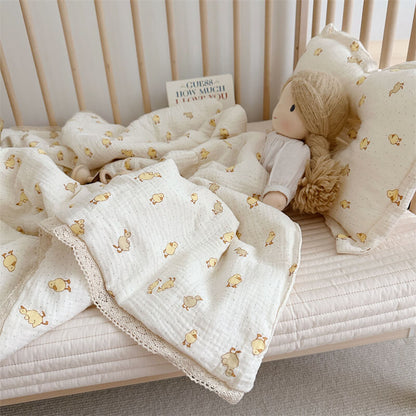 Baby crib with muslin blanket featuring yellow duct prints, plush toy, and pillow.