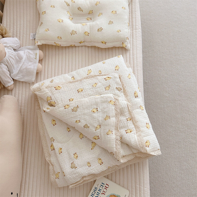 lightweight muslin baby quilt with duck design and pillow on the crib