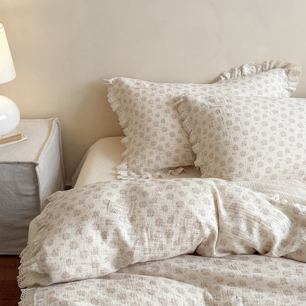 Side view of vintage French country style bedroom with dusty pink floral duvet cover, coordinating ruffled pillowcases, and an elegant bedside table lamp.