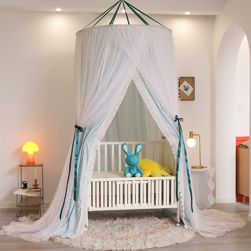 Toddler or baby bed canopy in blue-green print, suspended from the ceiling and draped open over a white wooden crib with a plush toy inside.