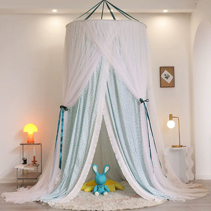Princess fabric bed canopy in blue-green floral print and sheer white netting, tied open to create a cozy play tent nook on a round white rug with a blue plush bunny toy inside.