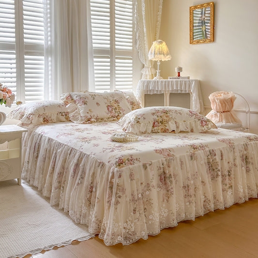 Floral bedspread on a bed in a well-lit bedroom with curtains and a lamp.