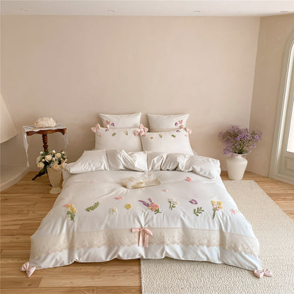 Ivory white floral embroidered bedding set with lace trim, raised flower details, and soft pink ribbon accents in a romantic teen bedroom