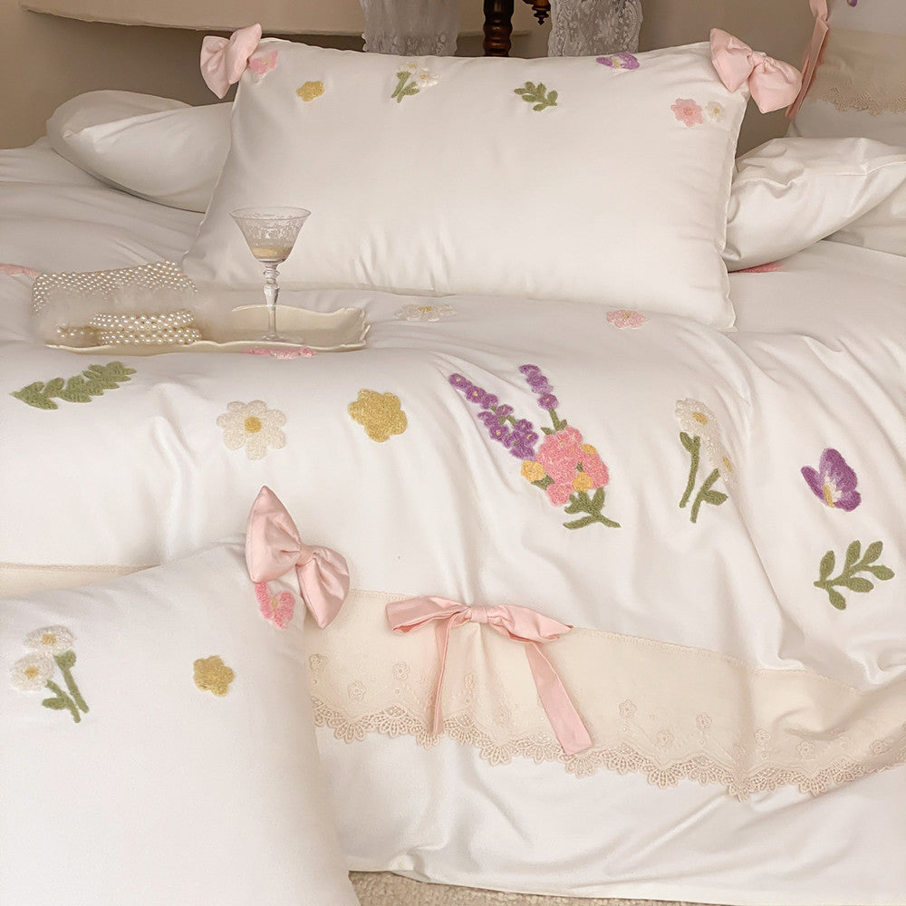 Close-up of ivory white bedding with raised floral embroidery, pink ribbon accents, butterfly motifs, and lace trim