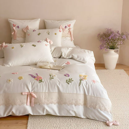 Ivory floral embroidered bedding set with delicate lace trim, pink bow accents, and decorative pillows for a teen bedroom