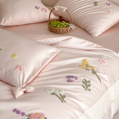 Close-up of blush pink bedding with raised floral embroidery, lace trim, butterfly motifs, and ribbon accents