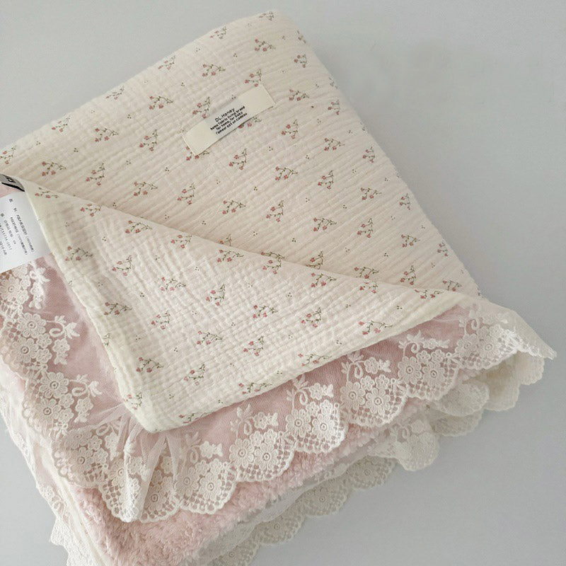 Folded cotton gauze comforter with small pink floral print, showcasing soft pink fleece lining and delicate lace ruffle edge.