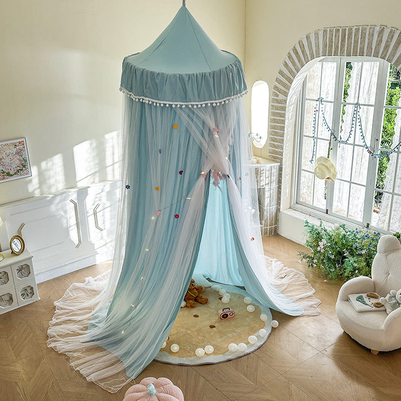 Full view of the Haze Blue kids canopy tent with pom-pom trim, set up as a play tent over a rug, featuring colorful sheer netting decorations and a wide draped design skirt.