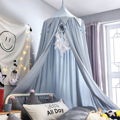 Light blue kids bed canopy with falbala ruffles and pom-poms, decorated with string lights and a dreamcatcher for a serene bedroom.