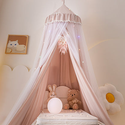 Close-up of a Pale Pink princess canopy with pom-pom trim, showing the sheer white mosquito netting and a mattress with stuffed animals inside, perfect for a baby or toddler nursery bed.