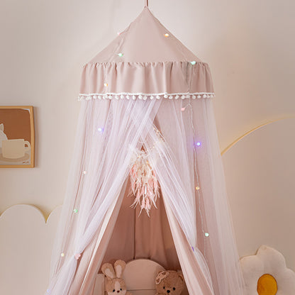Pale Pink kids princess canopy tent featuring a white pom-pom trim and multi-colored string lights, focusing on the soft solid fabric and sheer tulle layers for nursery decor.