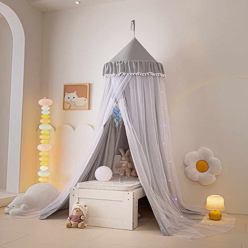 Gray children's bed canopy tent with white pom-pom fringe, providing a neutral and stylish hanging decor element for a modern kids' room, set up over a white storage bench.