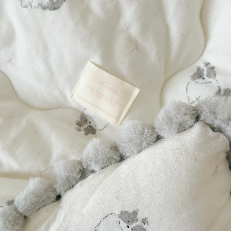 Close-up of the cat-print cotton comforter showing the gray pom-pom trim and fabric texture.