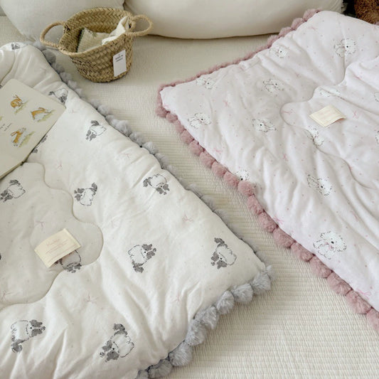 Two kids' comforters with pom-pom trim. One has a cat print with gray poms, the other has a dog print with pink poms.