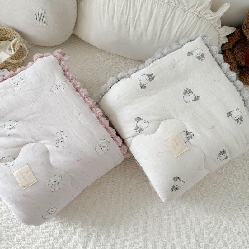 Kids' cotton comforters with pom-pom trim on a bed. One is pink with dog prints, the other is gray with cat prints.