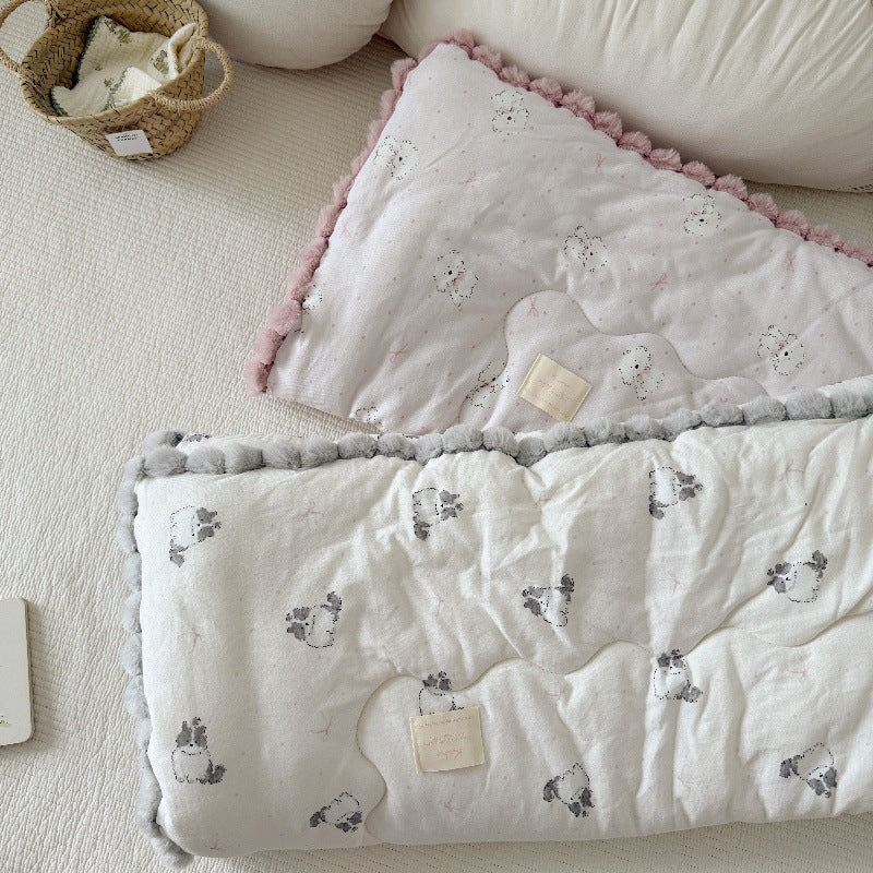 Overhead view of two kids' cotton comforters with pom-pom trim, one cat print with gray trim and one dog print with pink trim.