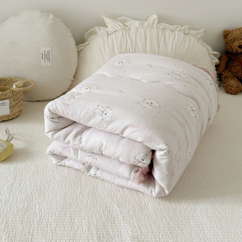 Kids' cotton comforter with dog print and pink pom-pom trim, neatly folded at the head of a bed.