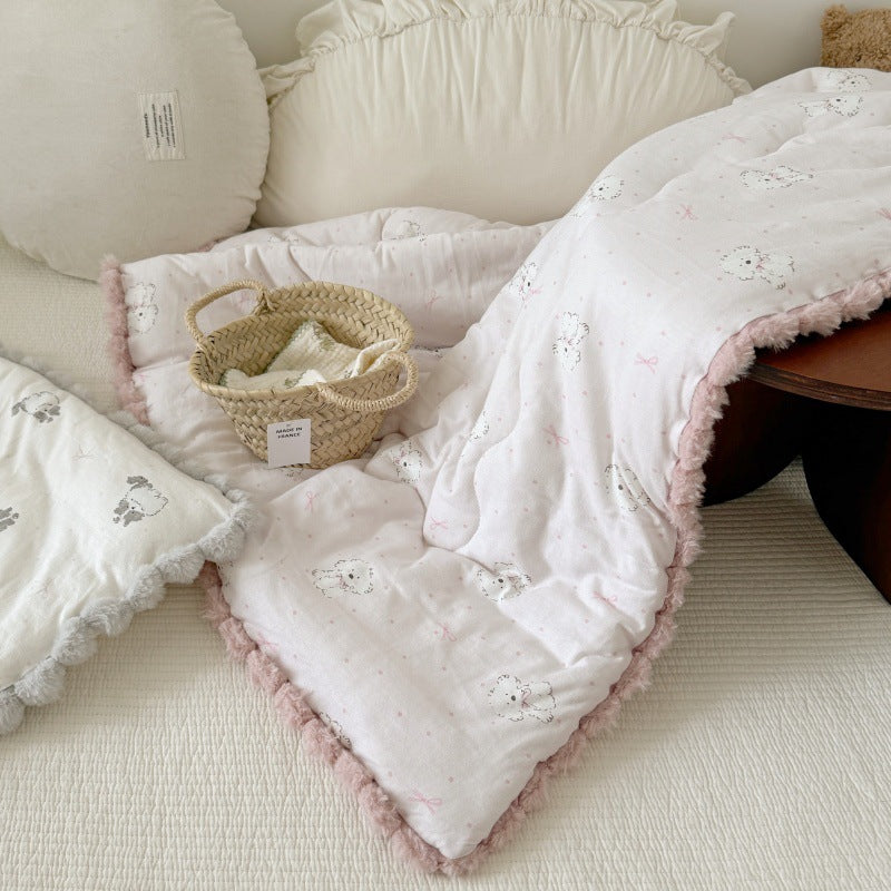 Kids' cotton comforters with pom-pom trim on a bed. Shows a pink dog-print and a gray cat-print version.