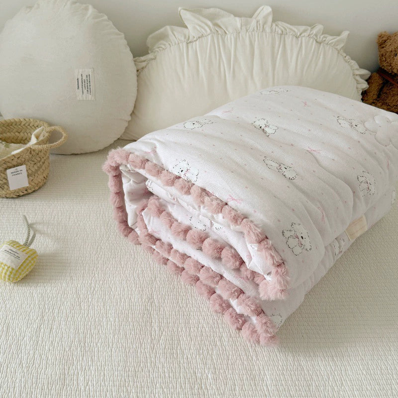Kids' cotton comforter with a dog print and pink pom-pom trim, neatly folded on a bed.