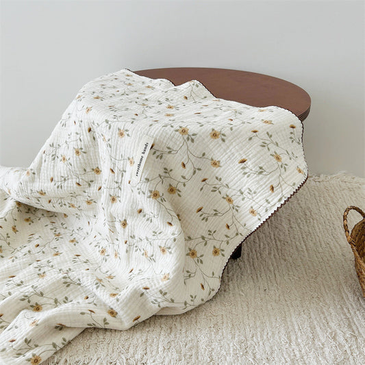 The yellow floral muslin baby blanket draped over a wooden table, showcasing the soft texture and pattern
