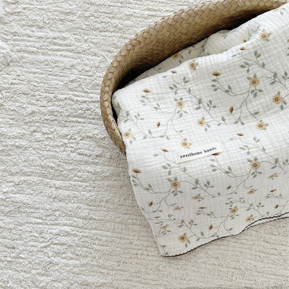 Yellow floral cotton muslin baby blanket folded neatly in a woven basket with the product label visible.