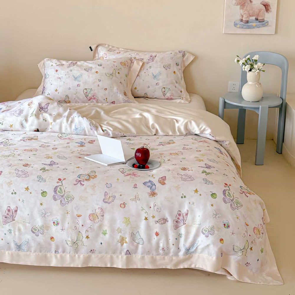 Full bed view of the champagne luxury Lyocell butterfly print bedding set, styled with an open white book and a plate of fresh red apples on the bed against a beige wall.