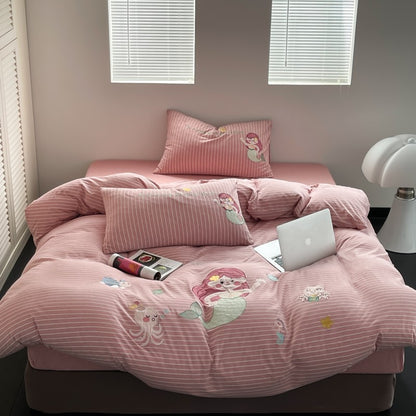 Pink bedspread with cartoon designs on a bed in a room with a lamp and window blinds.