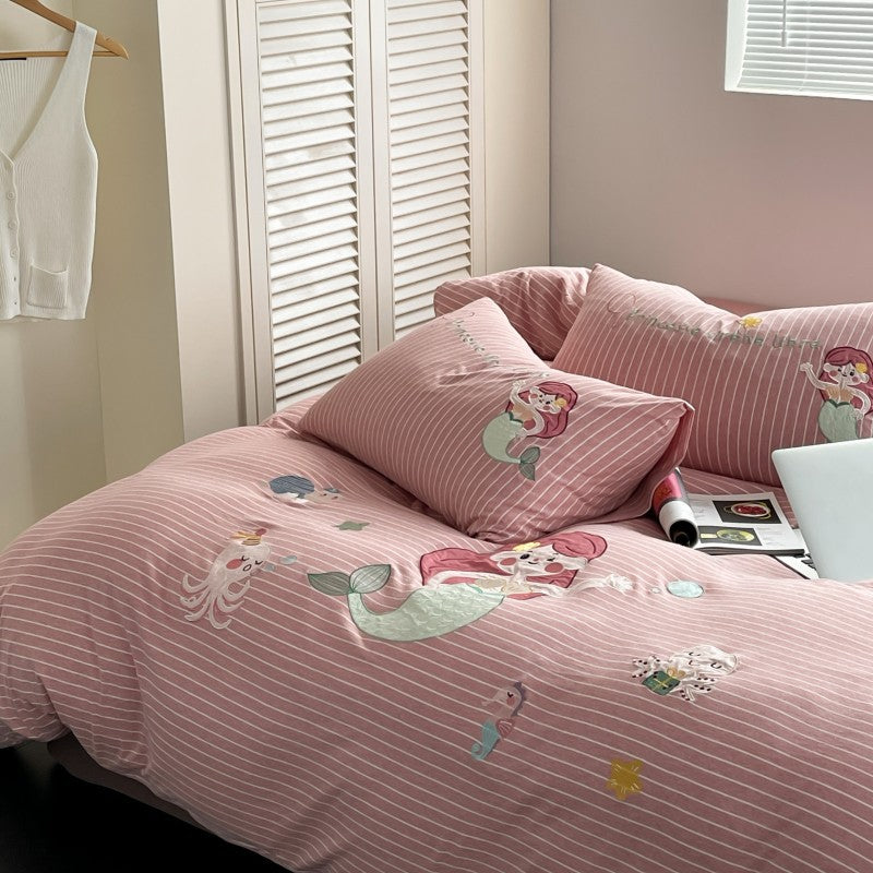 Pink striped bedding with mermaid designs on a bed in a room.