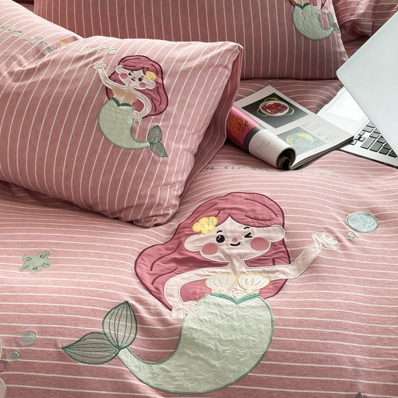 Pink striped bedding with mermaid design, laptop, and magazine on a bed.