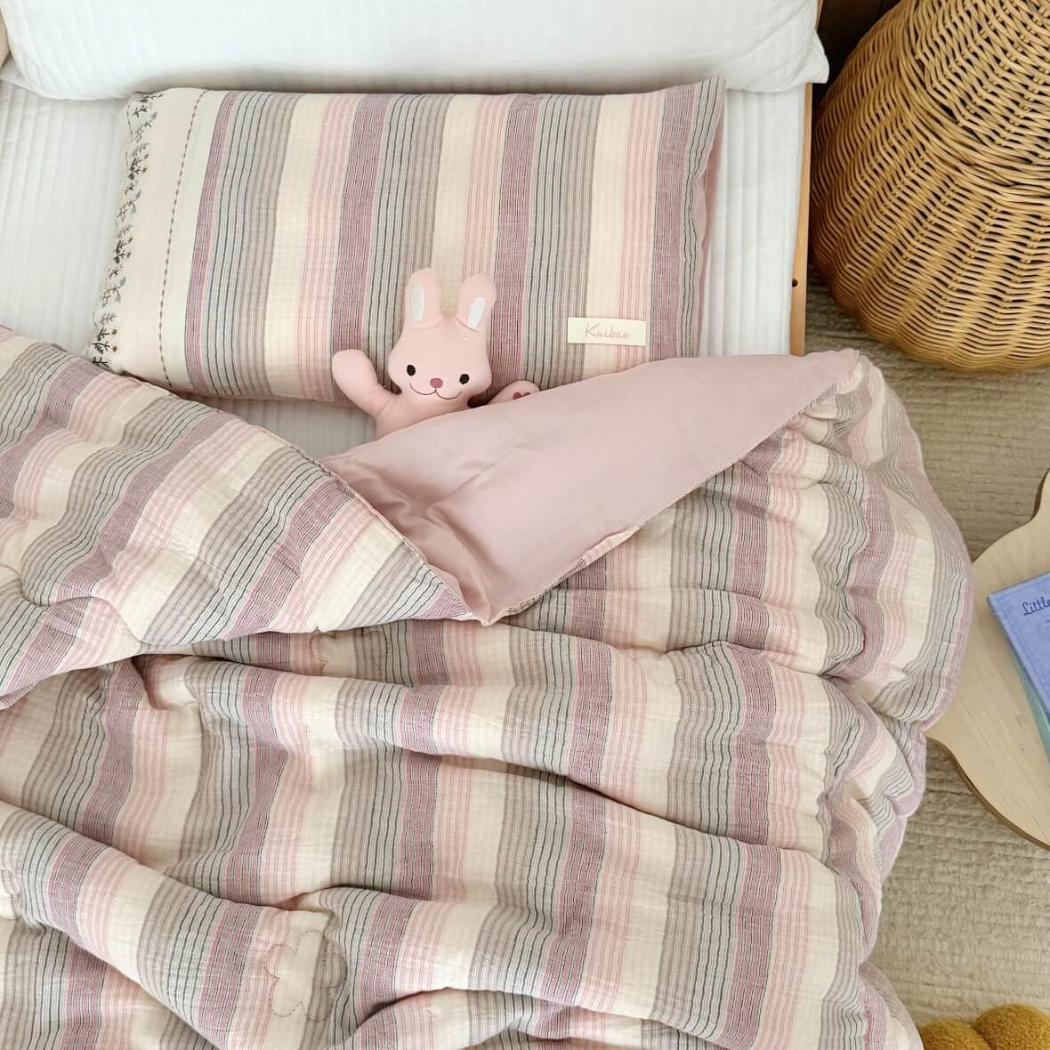Striped pink and purple comforter on a bed with a plush toy, in a cozy bedroom setting.