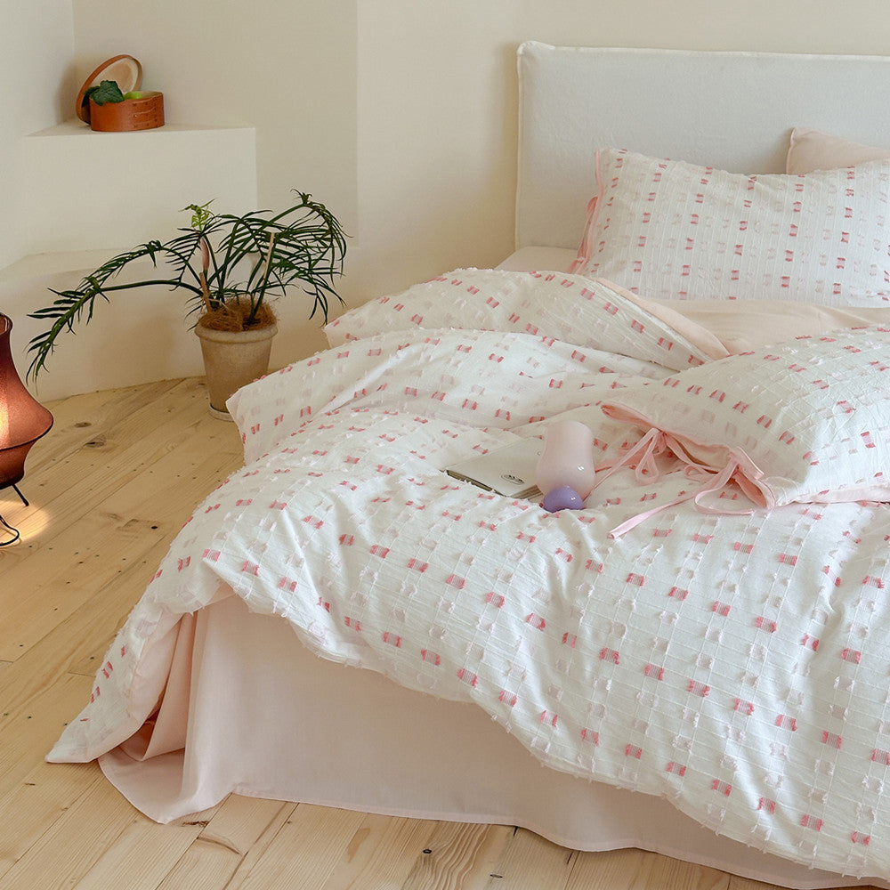 Pink Tufted Check Cotton Bedding Set on a bed, showing the textured duvet cover and blush pink bed skirt. The cozy cotton set features white fabric with a repeating pink tufted check pattern.