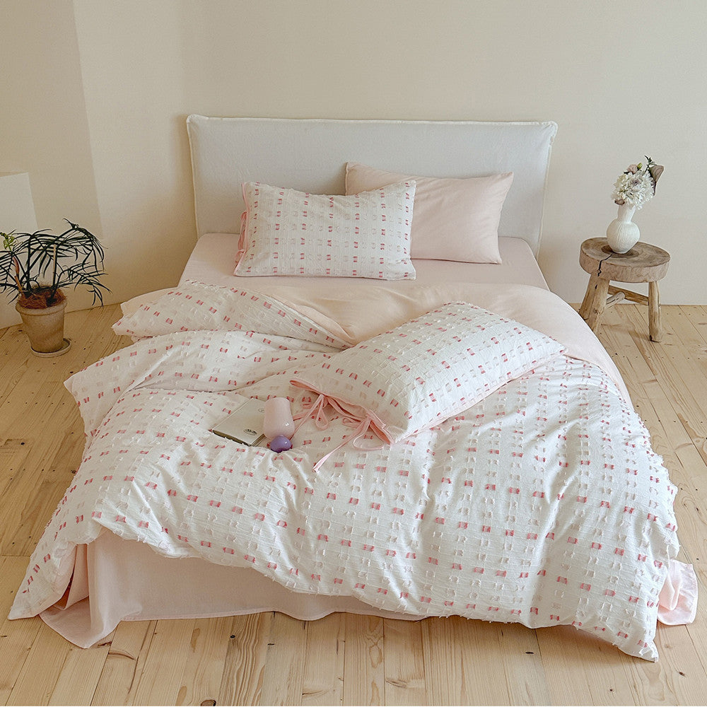 Full view of the Pink Tufted Check Cotton Bedding Set on a white headboard bed, highlighting the light pink fitted sheet, white tufted check duvet cover, and matching pink tie pillow shams in a bright, modern bedroom setting.