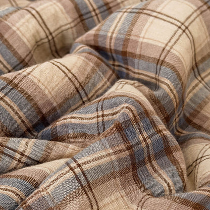 A close-up of draped plaid fabric with a warm beige base, brown stripes, and muted blue-gray lines.