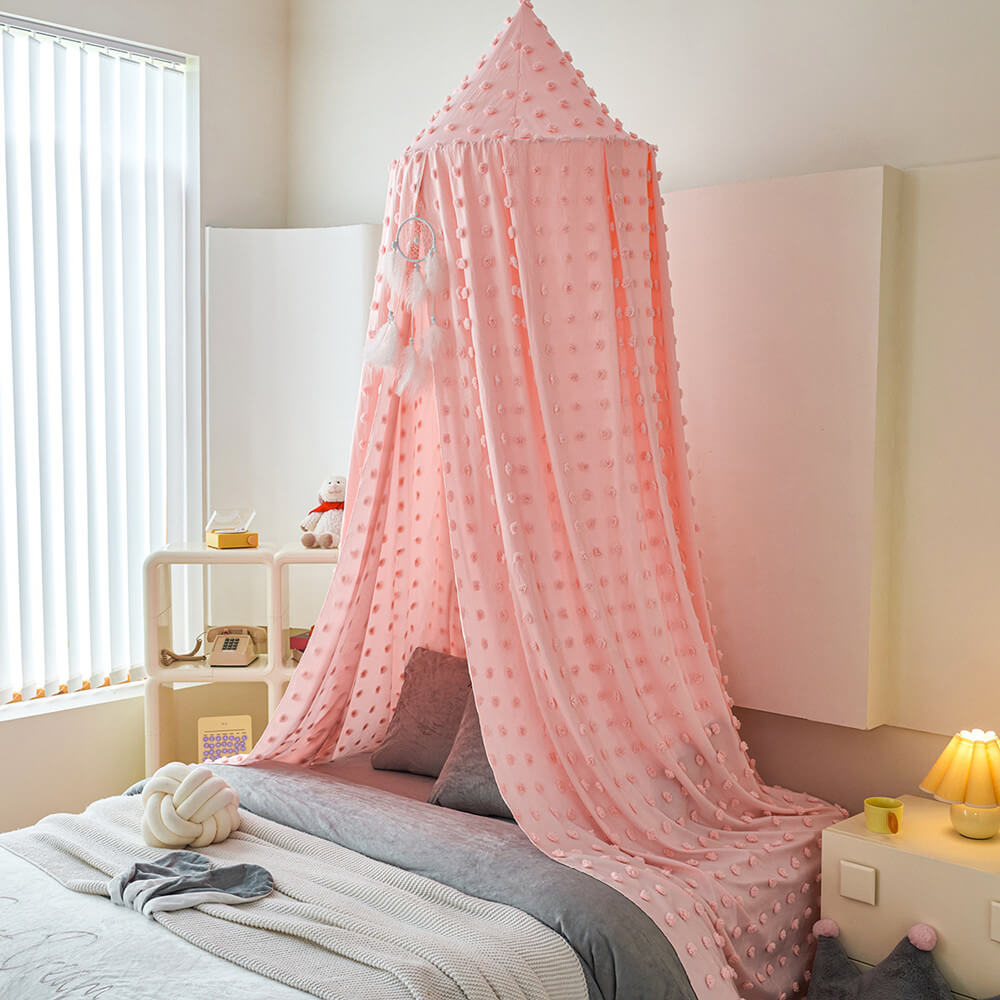 Blush pink pom pom kids bed canopy hanging beside a child’s bed
