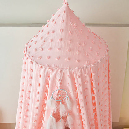 Pink canopy with pom-pom details and feathers against a white wall
