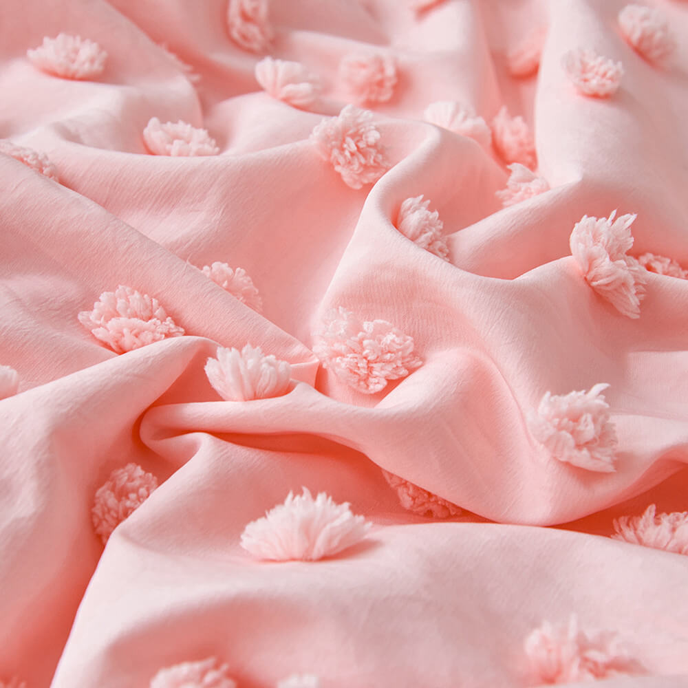 Close-up of blush pink polyester fabric with raised pom pom texture