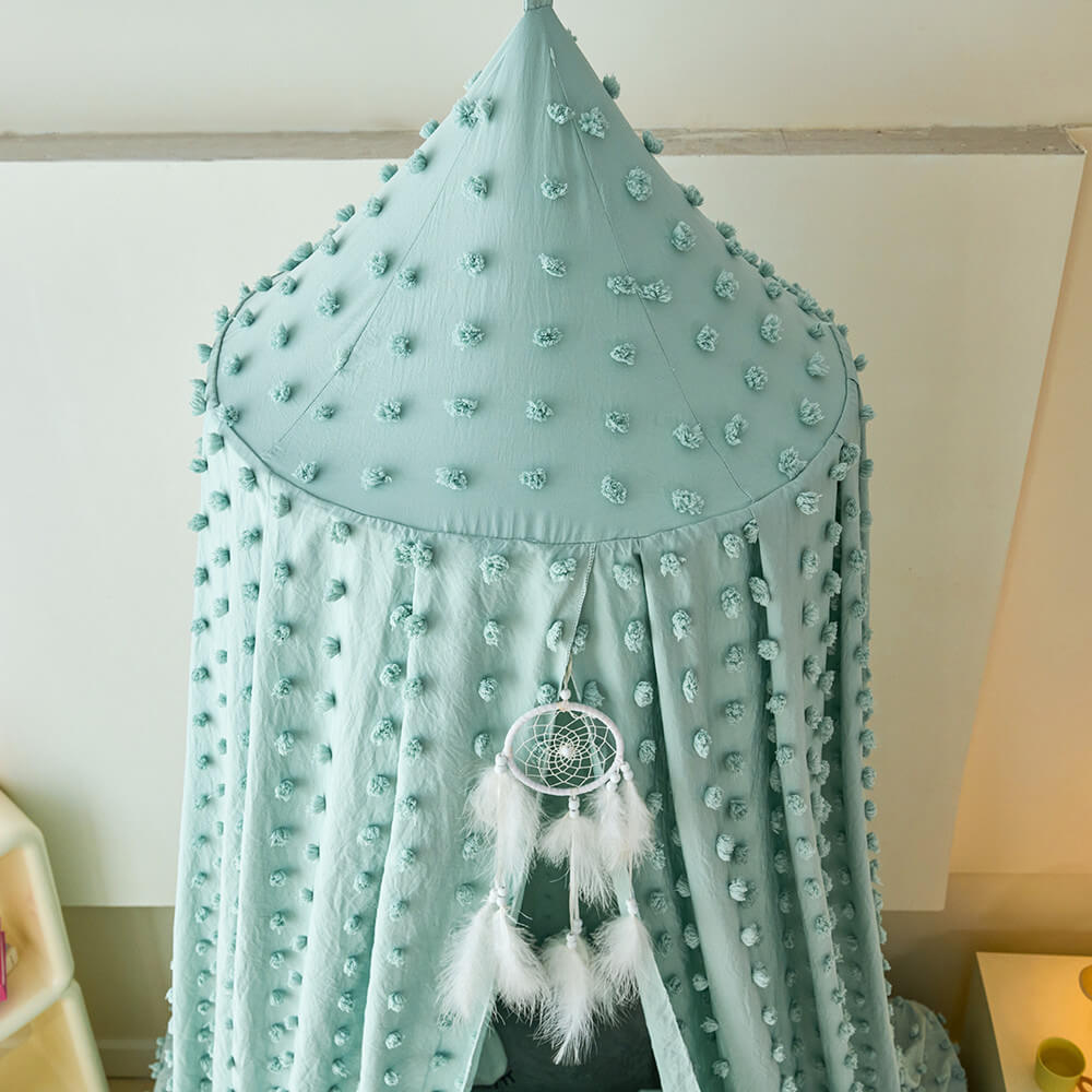 sage green canopy with pom-poms and a dreamcatcher hanging from it against a white wall.