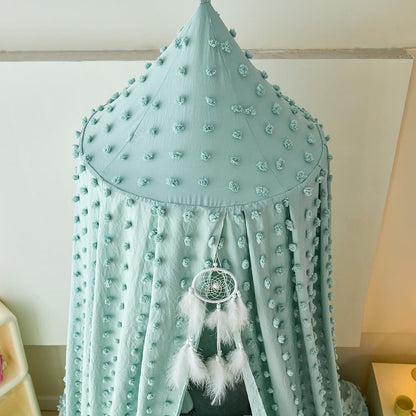 sage green canopy with pom-poms and a dreamcatcher hanging from it against a white wall.