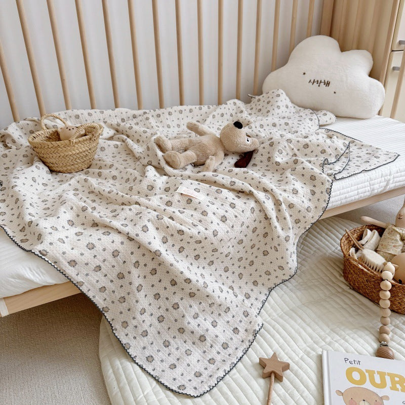 A pure cotton muslin blanket draped over a crib, with a toy basket and stuffed bear, showing its use in a nursery.