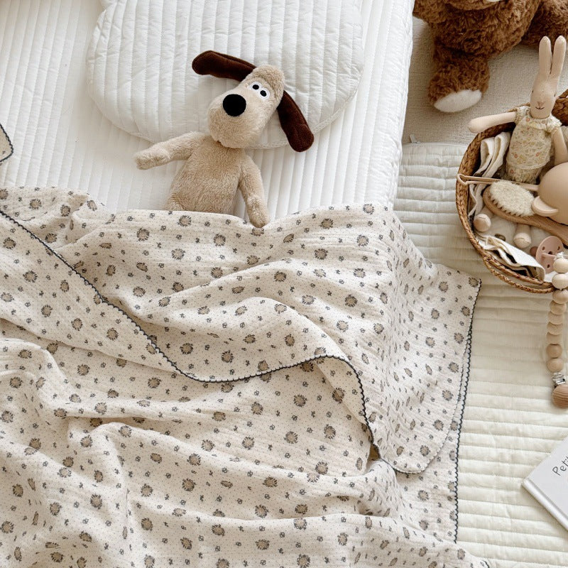 A close-up of a pure cotton muslin blanket tucked into a crib with a stuffed dog toy.